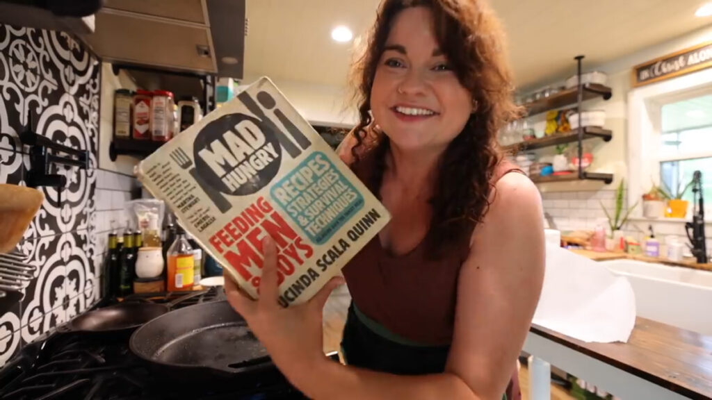 Woman holding up a cookbook called Feeding Men and Boys.