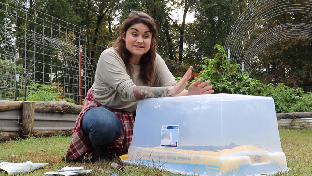 A woman crouched behind a bag of potting soil covered in a plastic tote.