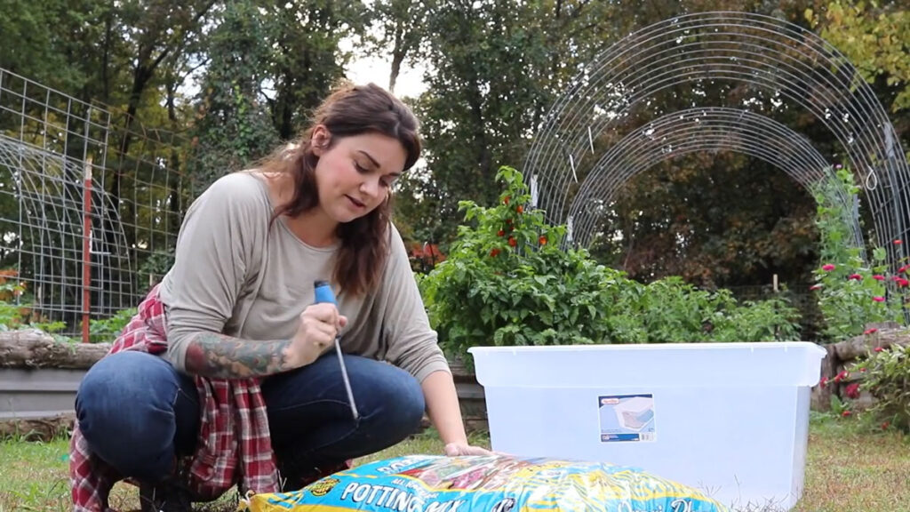 A woman piercing a bag of potting soil with a screw driver.