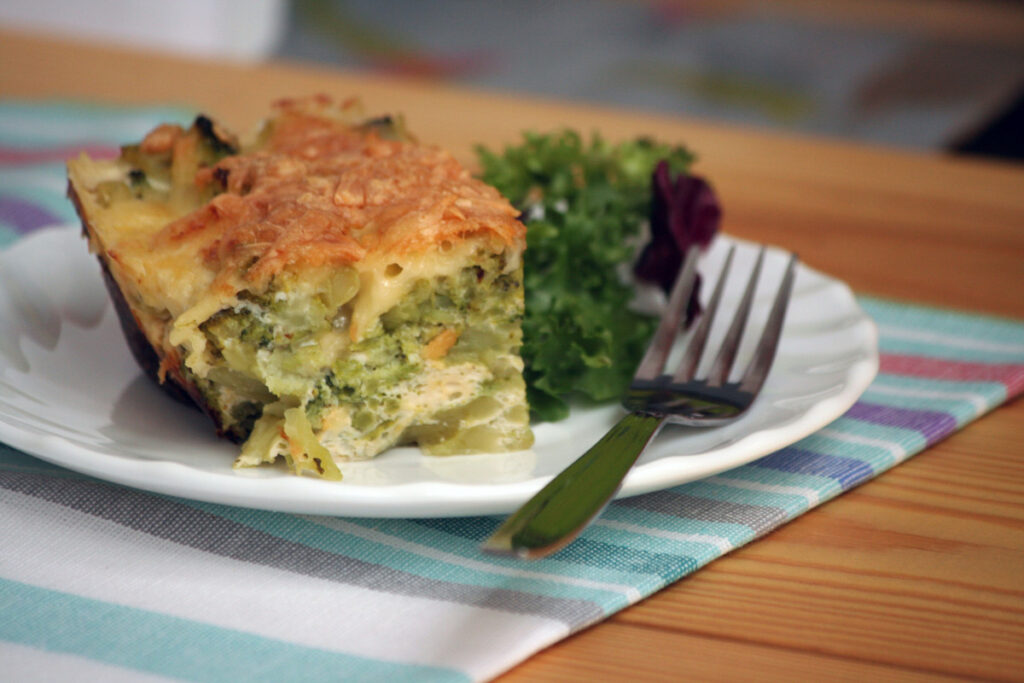 A slice of quiche on a white plate with fork.