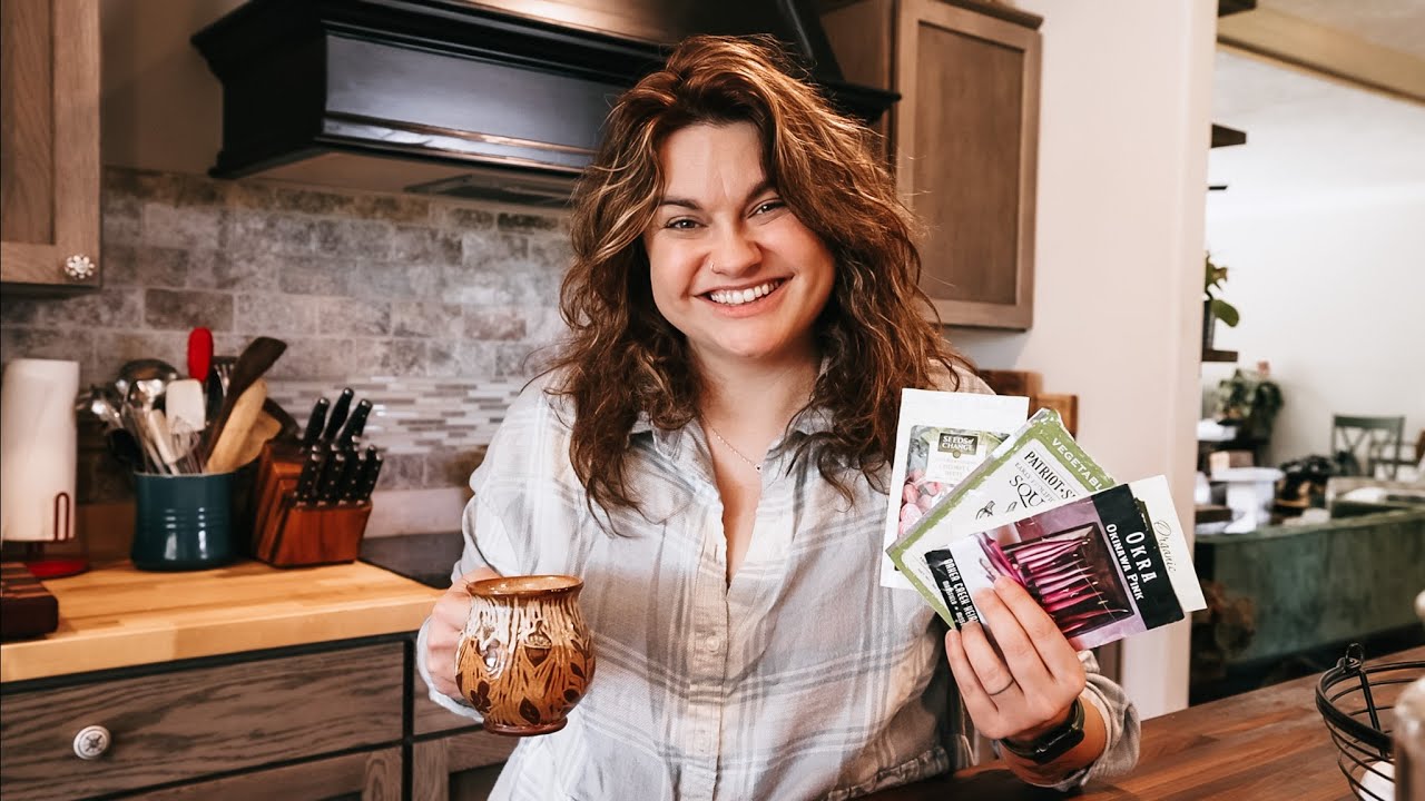 Woman holding seed packets and a cup of coffee.