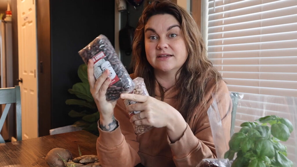 A woman holding up two bags of dry beans.