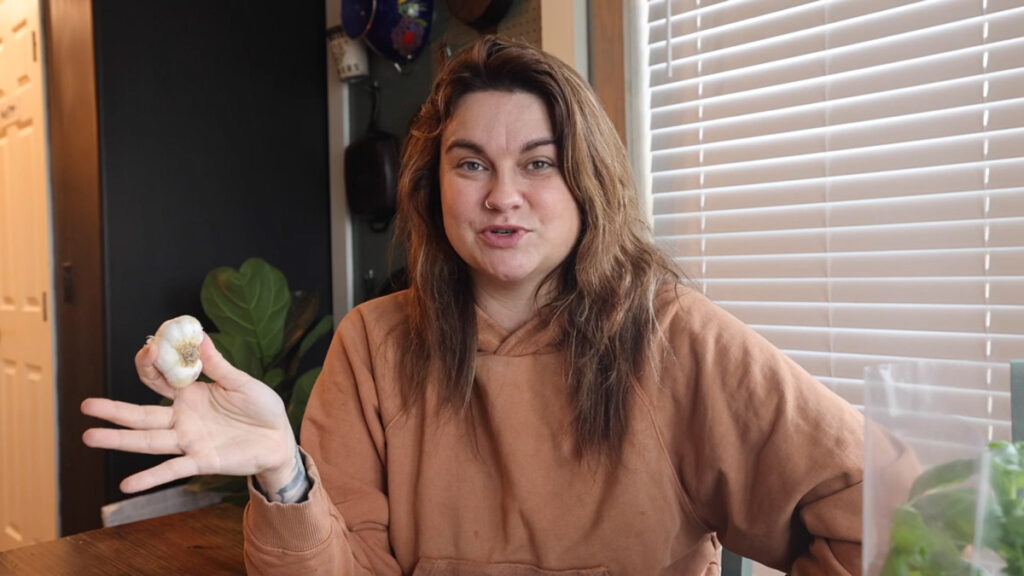 A woman talking and holding up a head of garlic.