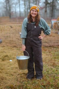A woman holding a pail of fresh raw milk in a field.