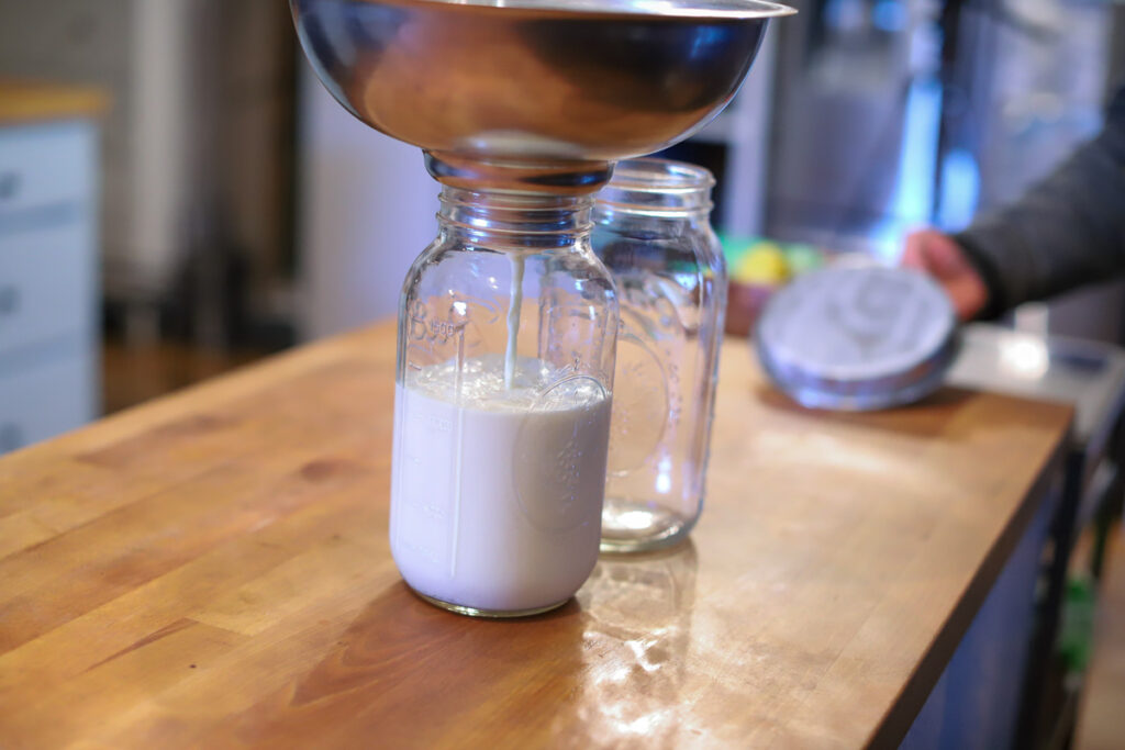 Raw milk being strained into a mason jar.