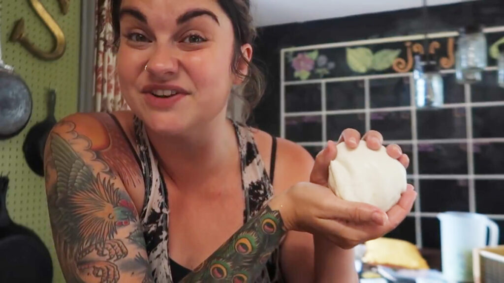 A woman holding up a fresh homemade mozzarella cheese ball.