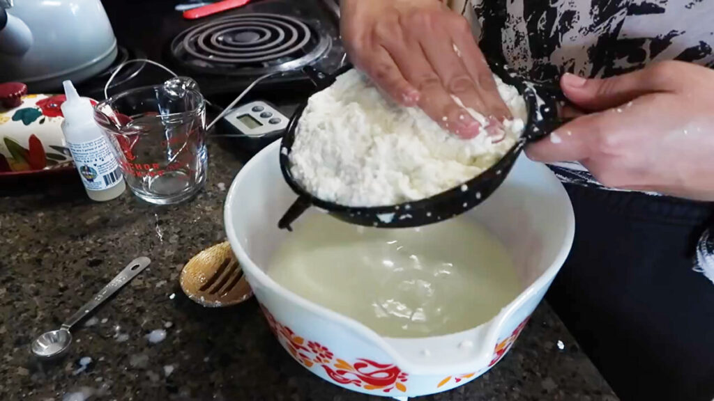 Pressing homemade mozzarella cheese curds through a colander.