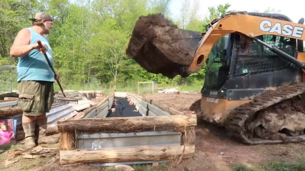 A backhoe dumping soil into a DIY raised garden bed.