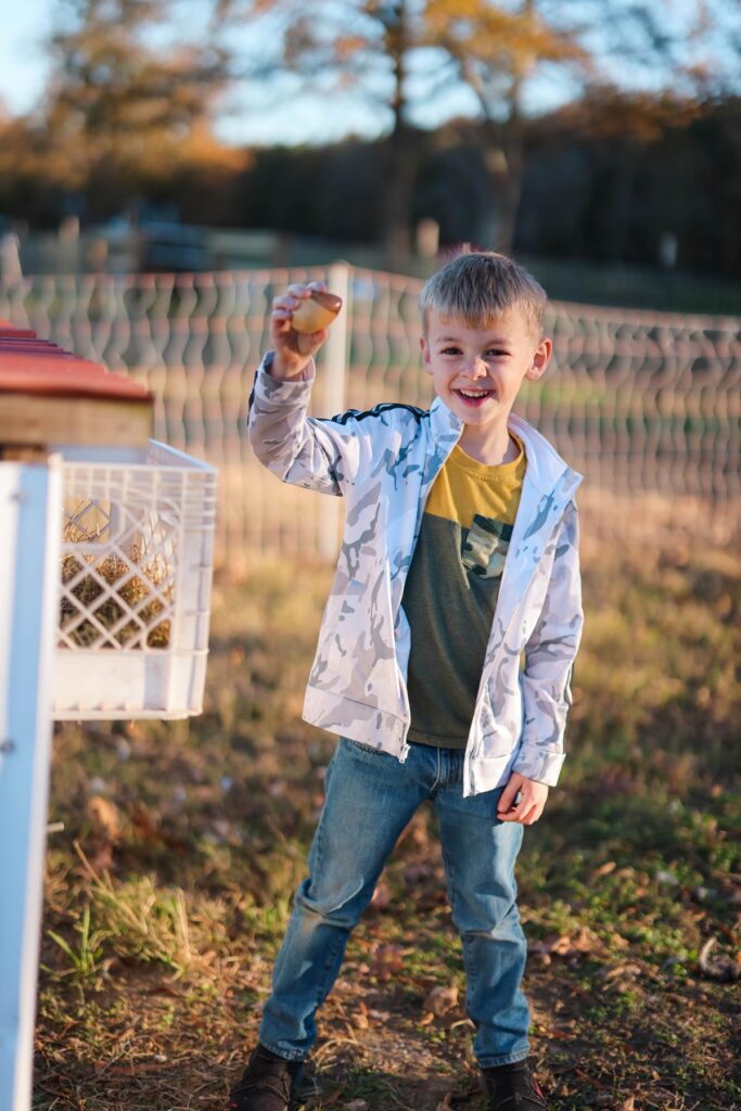 A young boy holding up a fresh egg from the chicken coop.