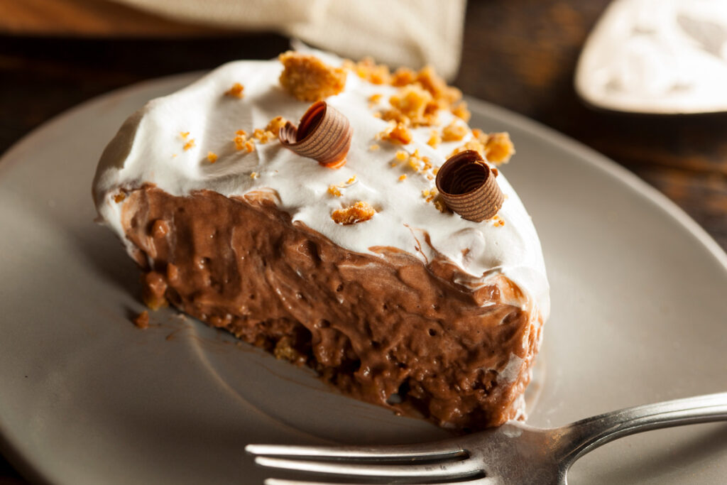 A slice of cocoa cream pie on a plate with a fork.