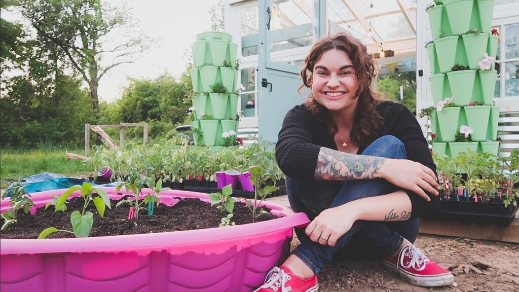 A woman sitting next to a kiddie pool turned garden bed.