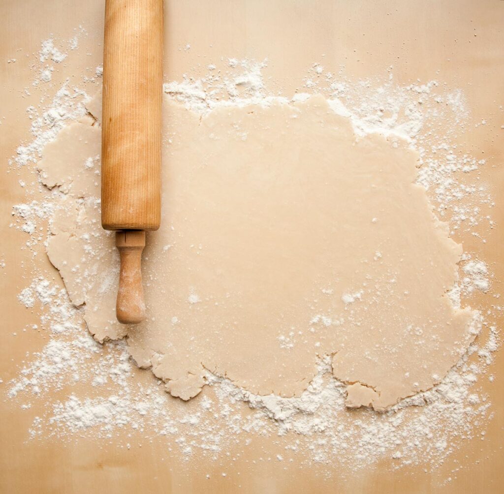 Pie crust rolled out on a floured surface with a rolling pin.