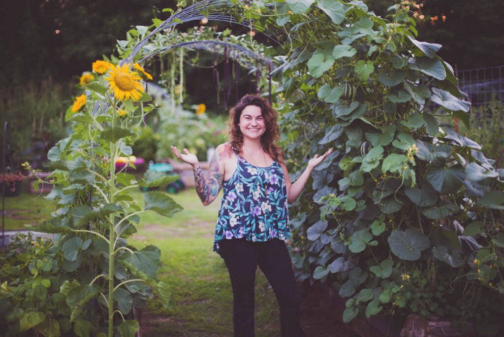 A woman standing under an arched trellis in the garden.