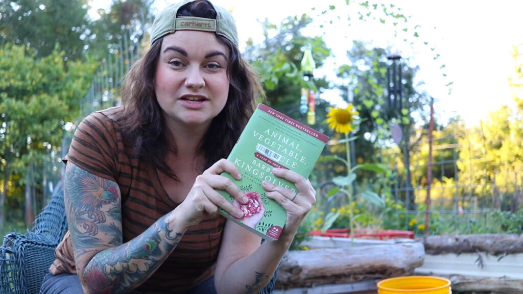 A woman in the garden holding up a book.