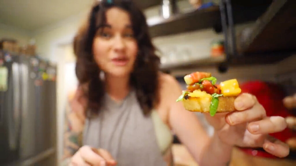 A woman holding up a piece of bruschetta before taking a bite.