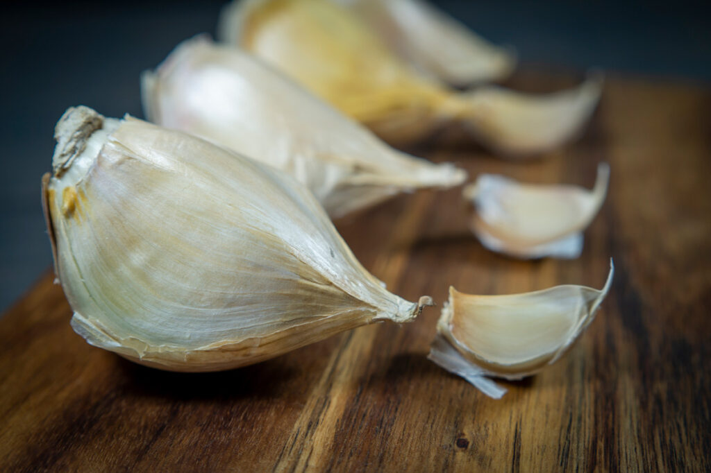 Elephant garlic cloves and regular garlic cloves on a wooden cutting board.