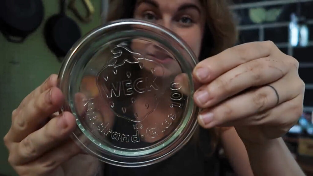 A woman holding up a glass weck jar lid.