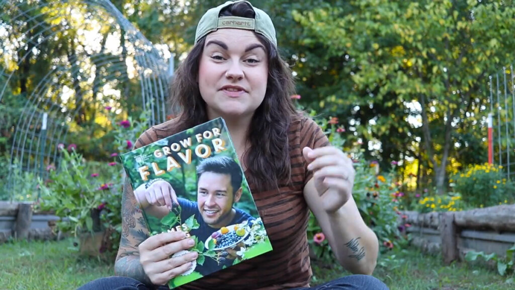 A woman in the garden holding up a book.