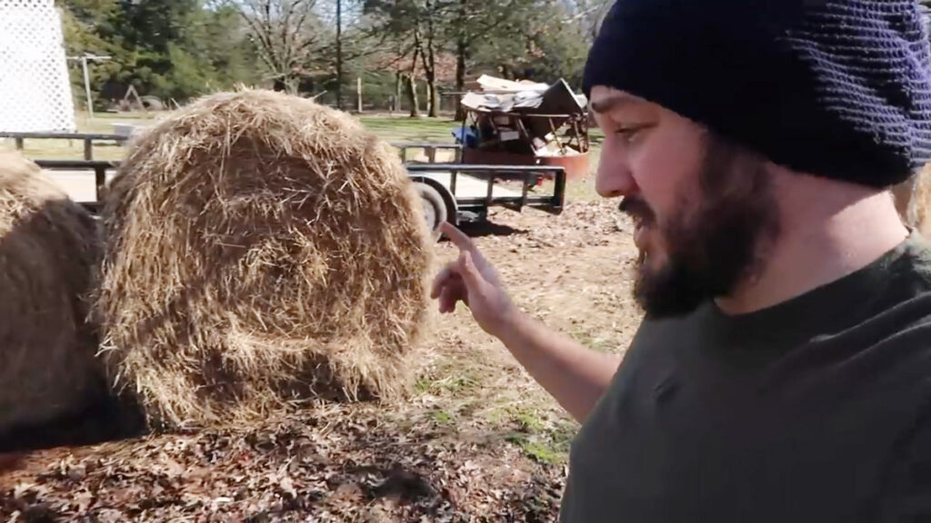 A man pointing to a large round bale of hay.
