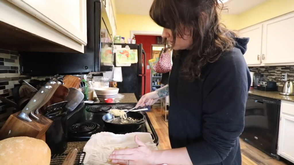 A woman spooning sauteed onions onto a tea towel.