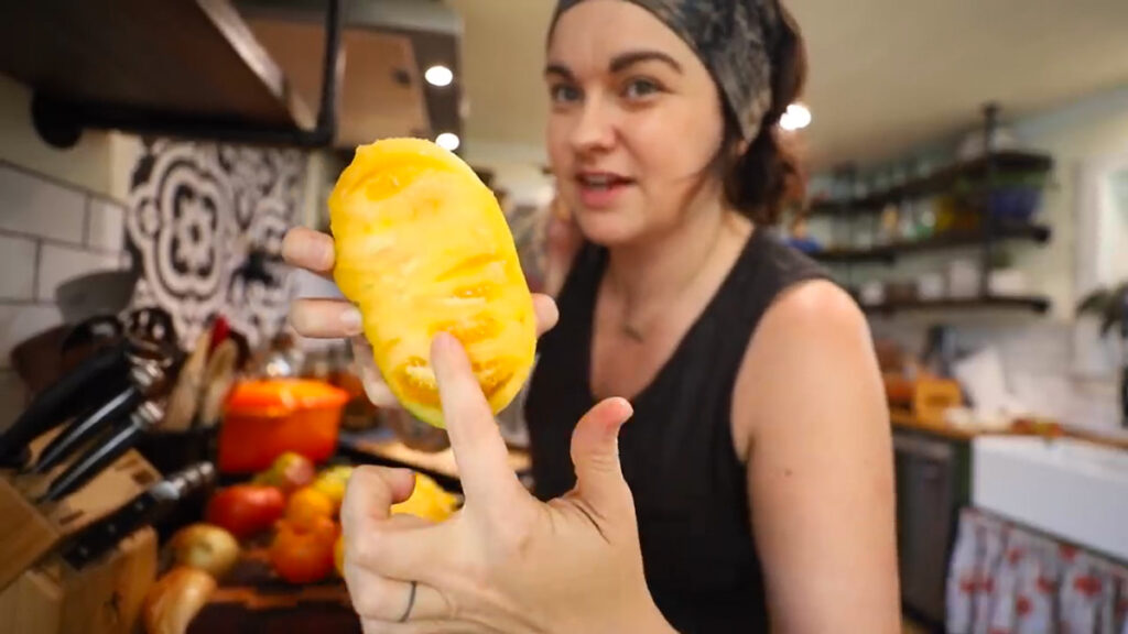 A woman pointing to the seeds of a sliced yellow tomato.