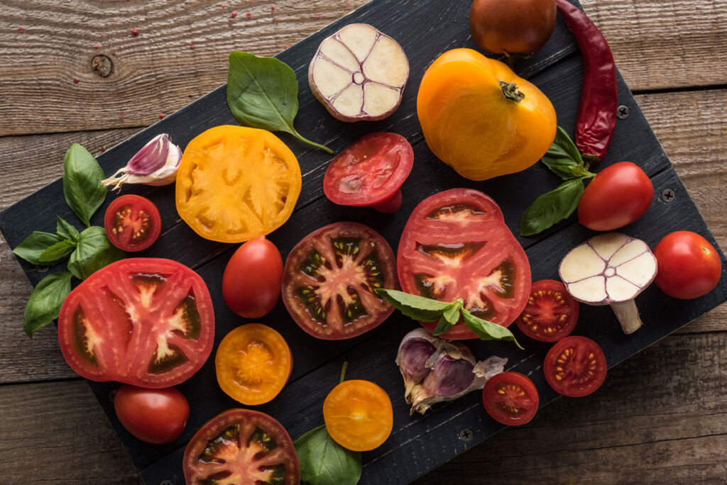 Sliced tomatoes, garlic and basil on a cutting board.