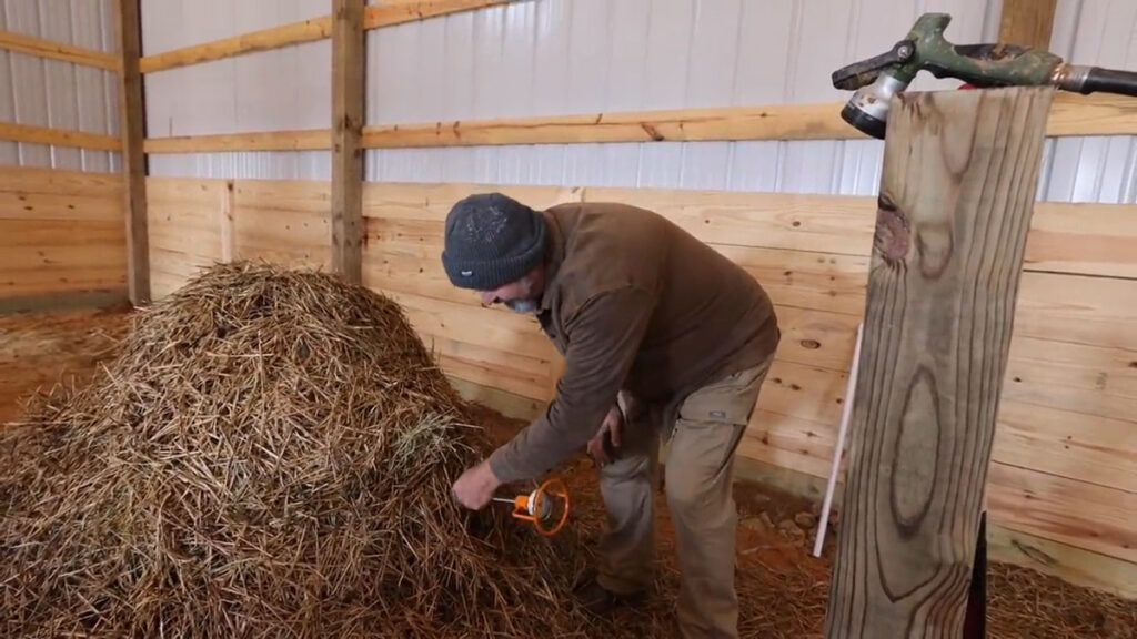 A man poking a thermometer into the center of a compost pile.