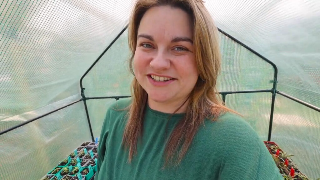 A woman standing inside a small greenhouse.