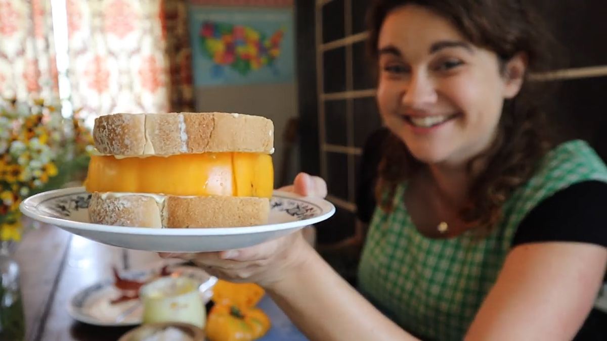 A woman holding up a tomato sandwich.