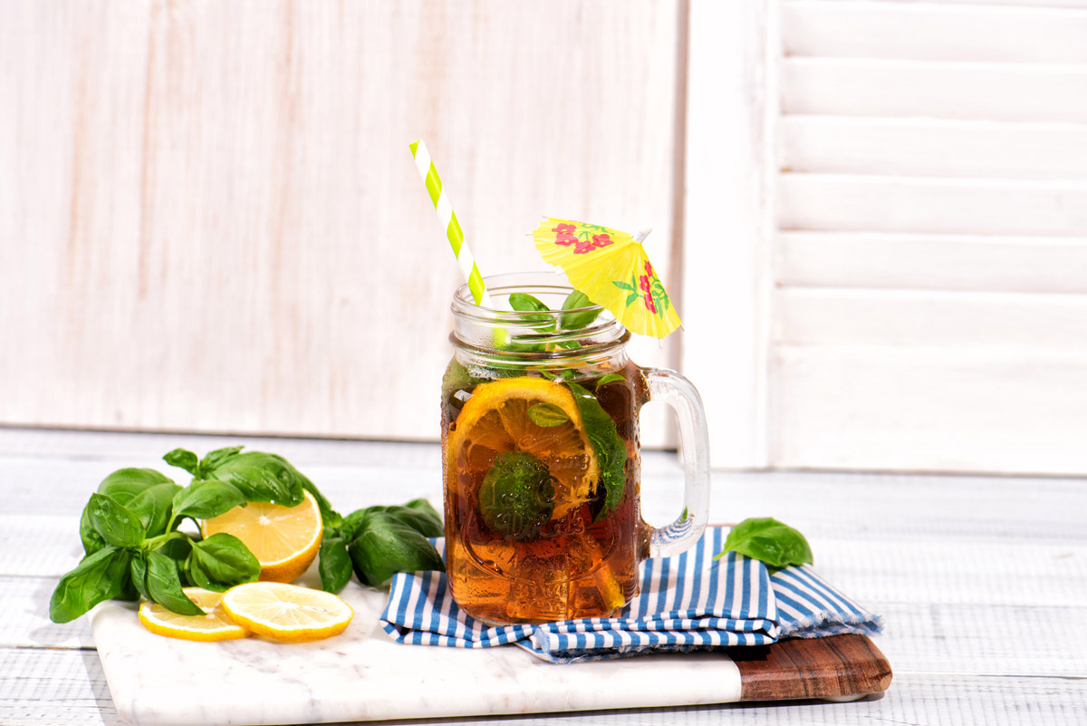 Basil iced tea in a glass with lemon wedges and fresh basil leaves.