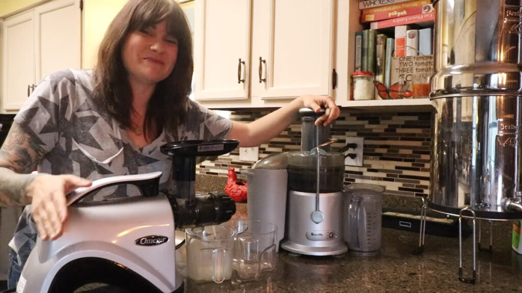 A woman standing next to two juicers in the kitchen.