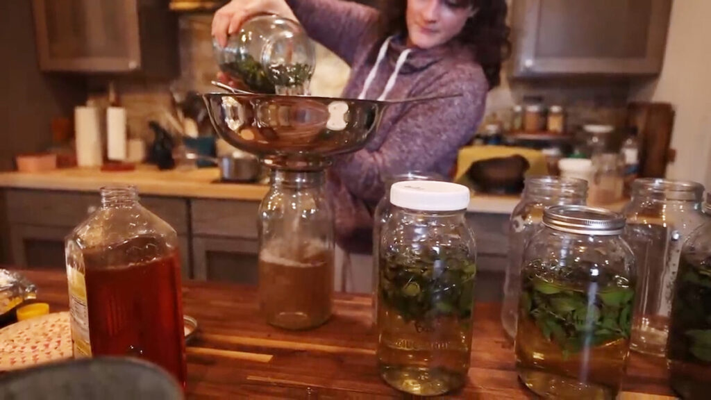 A woman pouring basil tea into a large jar.
