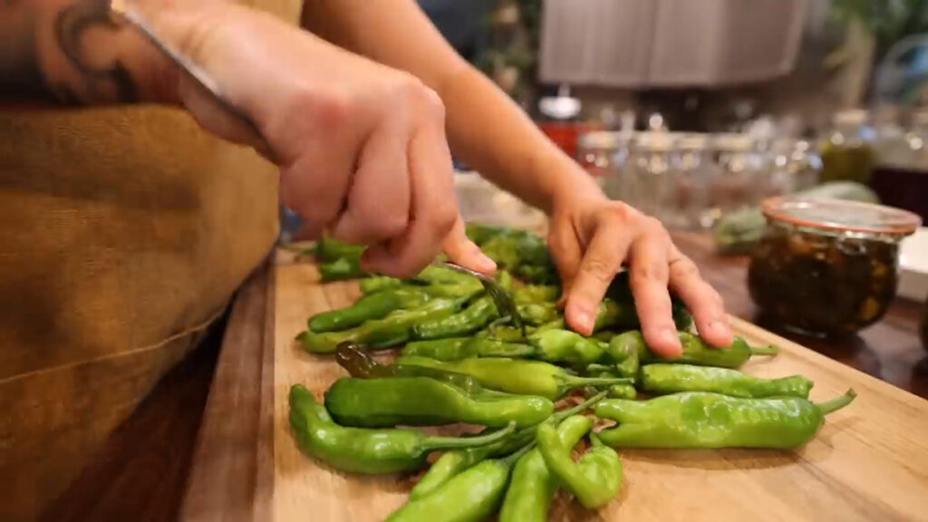 A woman poking shishito peppers with a fork.