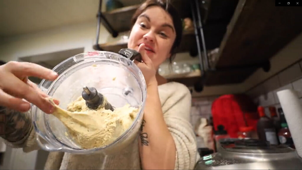 A woman holding up a food processor bowl with dumpling dough.