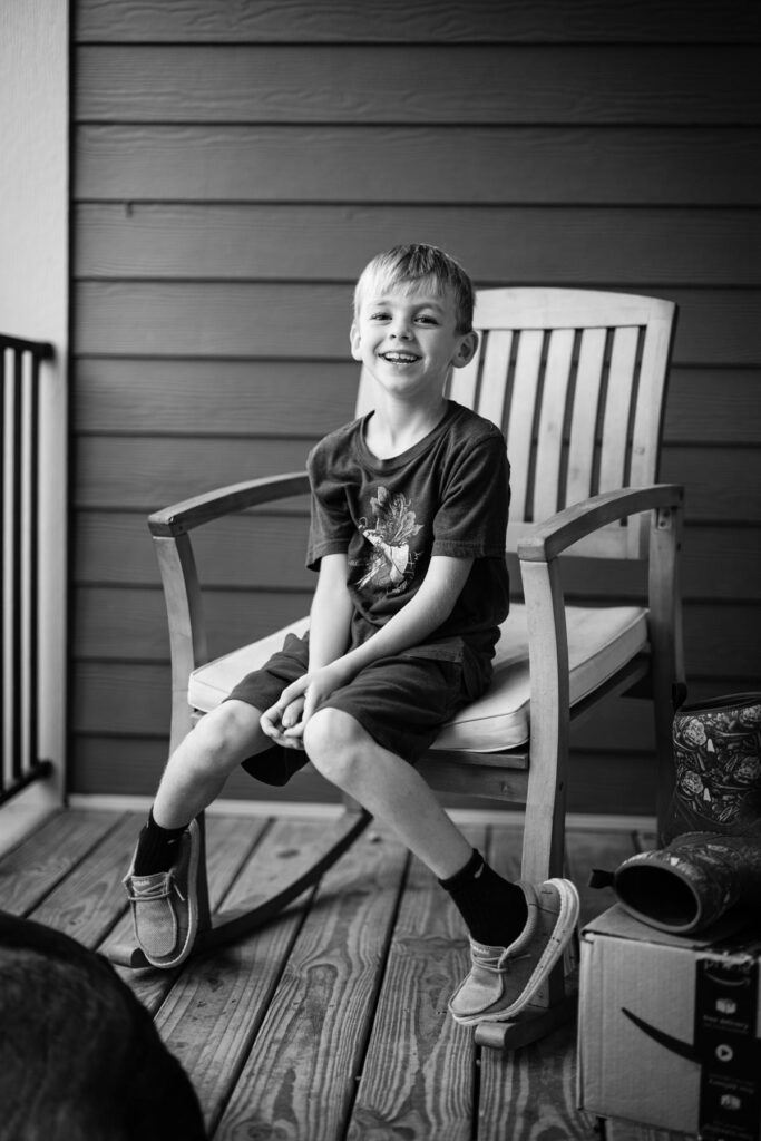 A young boy sitting in a rocking chair on a front porch.