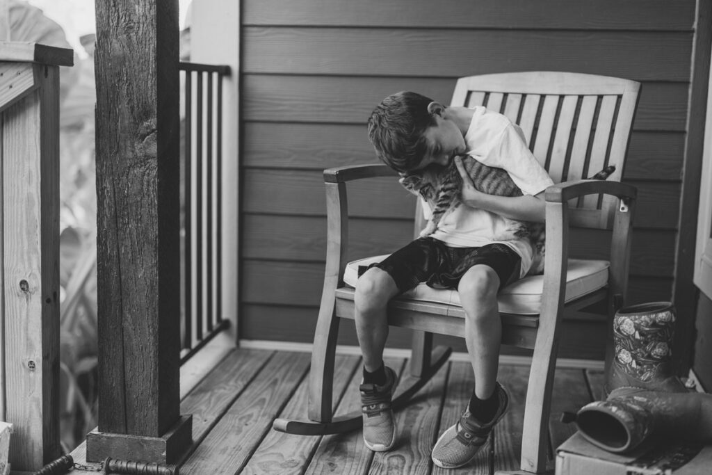 A young boy sitting in a rocking chair cuddling a cat.