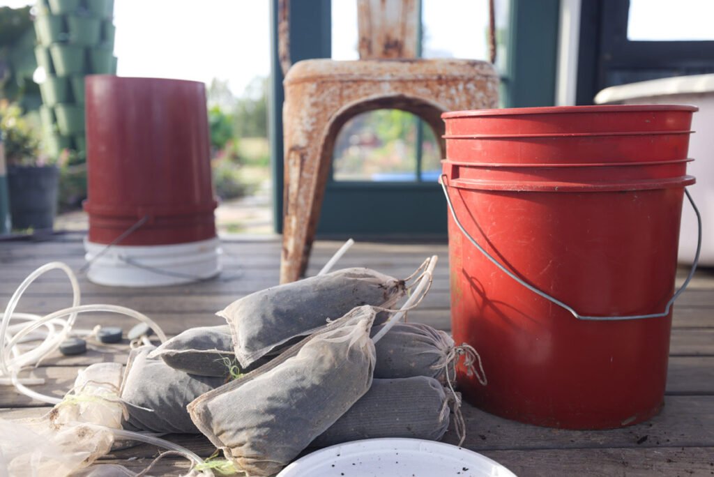 Multiple bags of compost tea next to a red bucket.