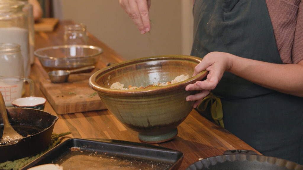 A woman adding rosemary to a bowl.