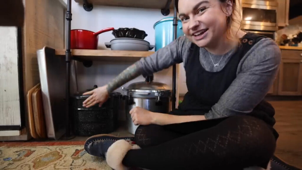 A woman pointing to a water bath and pressure canner on the shelf.