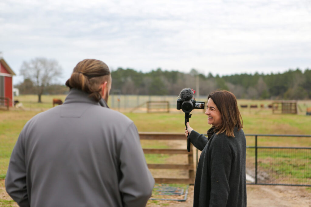 A man and woman talking to a camera while standing outside.