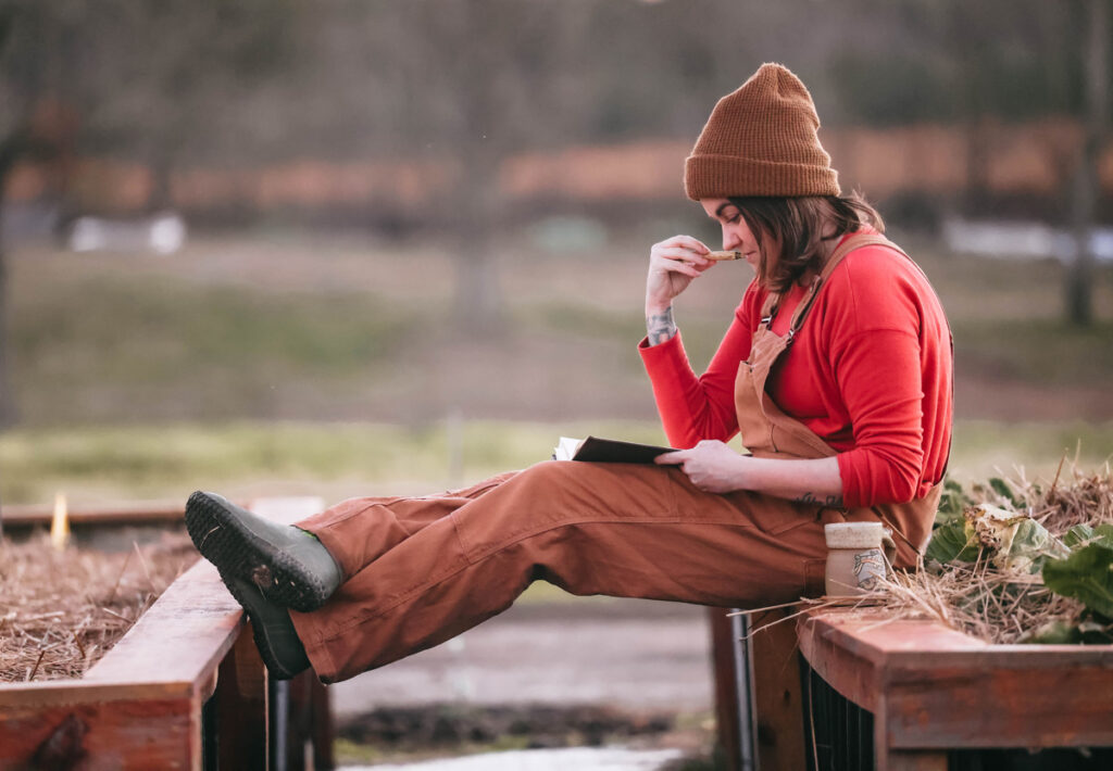 A woman sitting on a raised garden bed journalling.