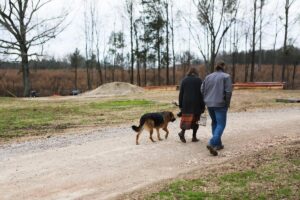 A man and woman walking down a dirt driveway with their dog following.