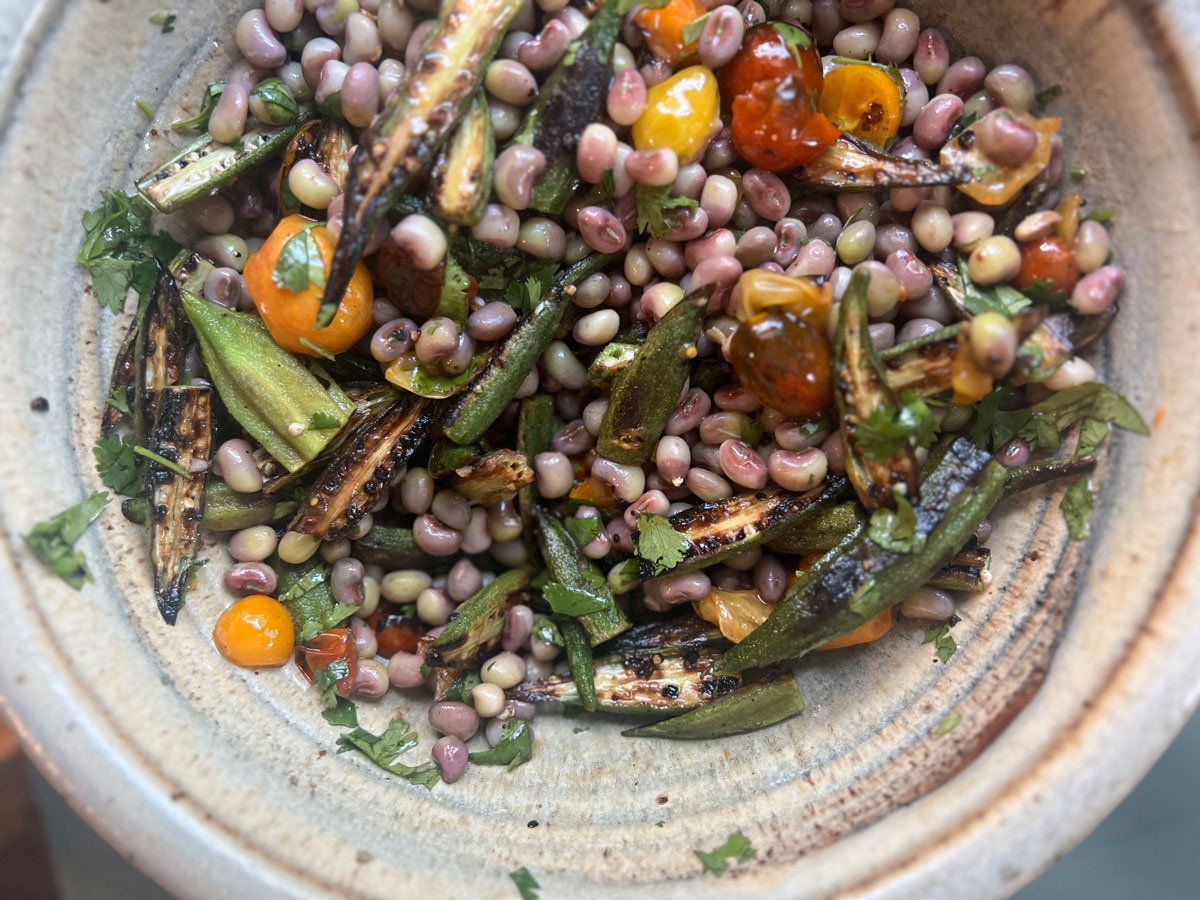 A large serving bowl with charred okra, tomatoes and field pea salad.